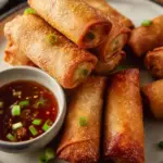 Crispy ground venison egg rolls served on a plate with dipping sauce.