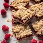 Homemade Raspberry Oatmeal Crumble Bars on a plate, topped with fresh raspberries.