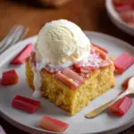 Delicious rhubarb cake topped with homemade rhubarb sauce on a white plate.